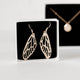 Handcrafted gold plated dangle dragonfly wing earrings by Krista Knickerbocker Designs in a white cardboard jewelry box with black felt in the background.
