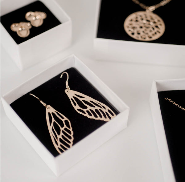Gold vermeil pieces by Krista Knickerbocker Designs in white cardboard boxes with black foam inserts.  Dragonfly wing earrings are in the forefront.