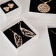 Gold vermeil pieces by Krista Knickerbocker Designs in white cardboard boxes with black foam inserts.  Dragonfly wing earrings are in the forefront.