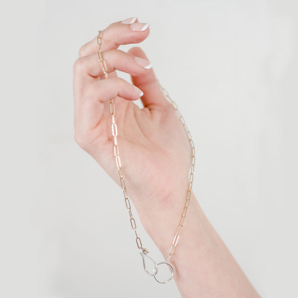 Woman's hand holding delicate gold filled elongated hoop chain with handmade sterling silver hook clasp.