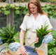 Beautiful woman arranging blue hydrangeas in a garden wearing a white shirt and tan apron and 14k gold water reflection handcrafted necklace by Krista Knickerbocker Designs.