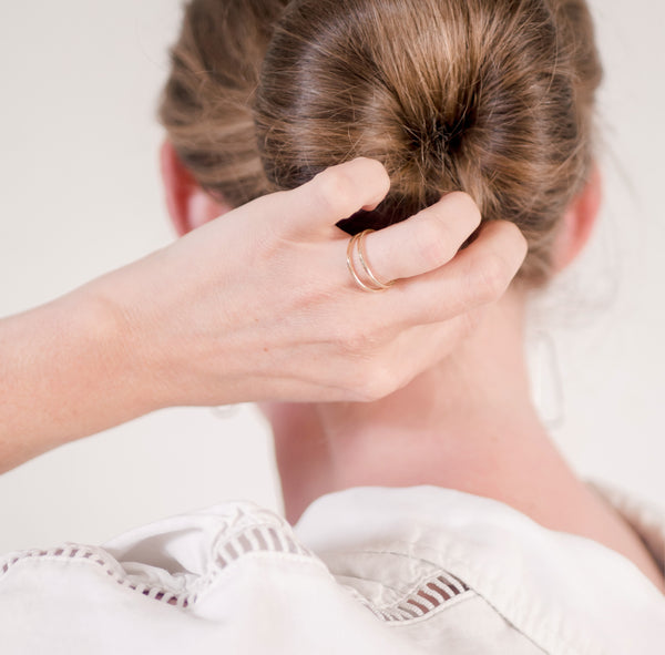 The back of a woman's head with a clean bun and her hand touching her hair while wearing a handcrafted double band gold vermeil ring by Krista Knickerbocker Designs.