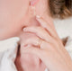 Close up of a woman's hands and earlobe in front of a white wall wearing a white shirt and handcrafted circle dangle earrings and double band vermeil ring by Krista Knickerbocker Designs.