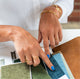Close up of a woman's hands pointing at fabric swatches with a blue manicure and white shirt on.  She is wearing handcrafted gold bangles and handcrafted double band rings by Krista Knickerbocker Designs.