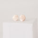 Close up of a pair of shiny, textured circular handcrafted gold post earrings on a white box by Krista Knickerbocker Designs.