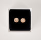Close up image of shiny, textured gold handcrafted circle stud earrings on a black velvet backing in a white cardboard jewelry box by Krista Knickerbocker Designs.