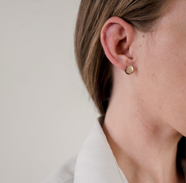 Closer up of woman's ear wearing gold, shiny, textured handcrafted "stardust" earrings by Krista Knickerbocker Designs.