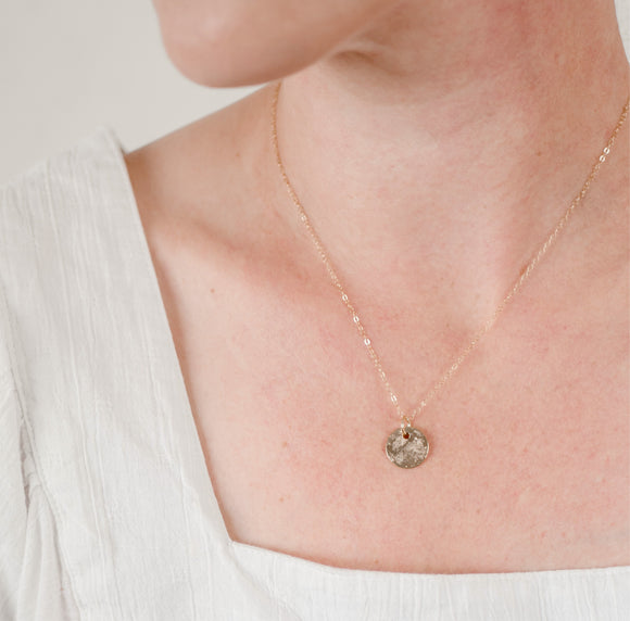 Close up of woman's neck wearing a dainty textured handcrafted 14k gold vermeil circle pendant necklace by Krista Knickerbocker Designs.