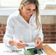 Beautiful smiling woman wearing a button up white collared shirt and considering fabric samples.  She is wearing a shiny gold handcrafted chunky chain necklace by Krista Knickerbocker Designs.