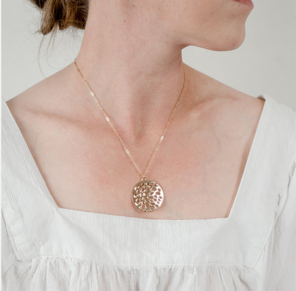 Zoom in of woman in a white top in front of a white wall wearing large 14k gold vermeil porous double layer handcrafted Water Reflection pendant by Krista Knickerbocker Designs. 