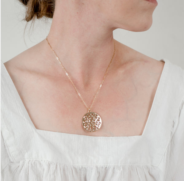 Zoom in of woman in a white top in front of a white wall wearing large 14k gold vermeil porous double layer handcrafted Water Reflection pendant by Krista Knickerbocker Designs.