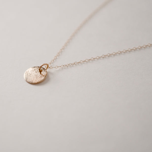 Close up of textured circle gold vermeil pendant hanging from dainty gold filled chain on a white background.  Handcrafted by Krista Knickerbocker Designs.