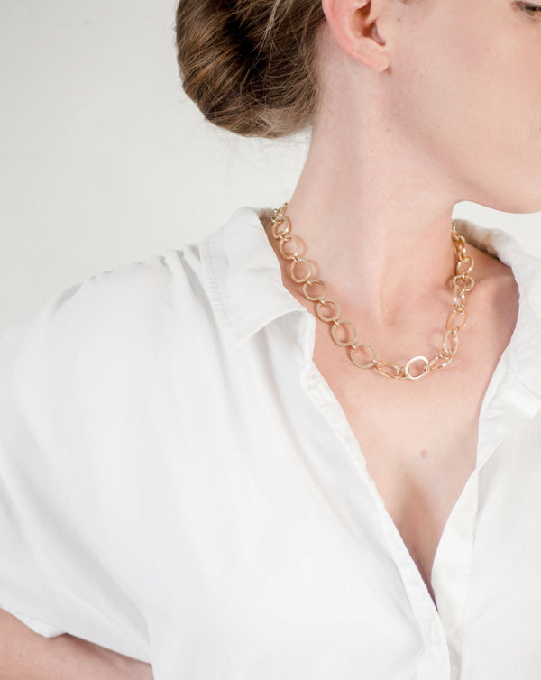 Woman in a white button down collared shirt in a confident power pose wearing a shiny gold handcrafted chunky chain by Krista Knickerbocker Designs.