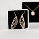 Handcrafted gold plated dangle dragonfly wing earrings by Krista Knickerbocker Designs in a white cardboard jewelry box with black felt in the background. 