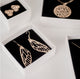 Gold vermeil pieces by Krista Knickerbocker Designs in white cardboard boxes with black foam inserts.  Dragonfly wing earrings are in the forefront. 