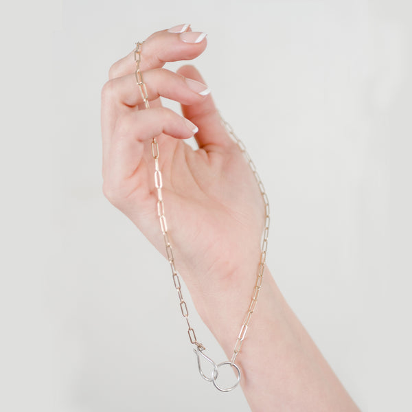 Woman's hand holding delicate gold filled elongated hoop chain with handmade sterling silver hook clasp.