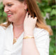 Beautiful redheaded woman smiling in a garden  and stroking her hair while wearing handcrafted gold vermeil jewelry by Krista Knickerbocker Designs. 