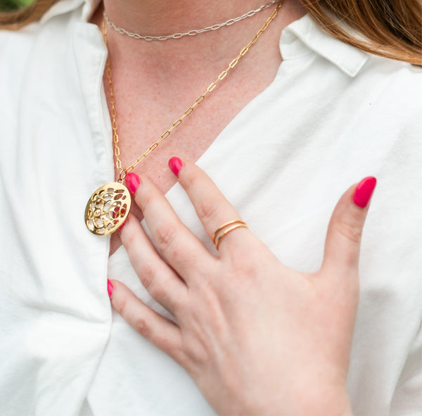 Close up of woman wearing a white shirt with a pink manicure and wearing handcrafted gold vermeil jewelry by Krista Knickerbocker Designs including the Water Reflection circular double layer pendant and the handcrafted double band ring. 