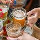 Close up of a group of woman's manicured hands holding glass beer glasses in a "cheers" motion.  Hand in focus is wearing a handmade Krista Knickerbocker Designs gold vermeil double band ring. 