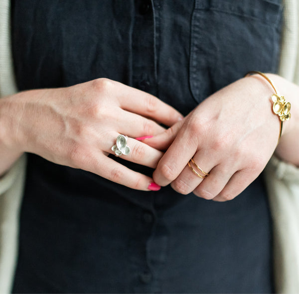 Close up of woman's hands with a pink manicure and handcrafted jewelry, including a sterling silver cluster ring and double band vermeil ring both by Krista Knickerbocker Designs. 