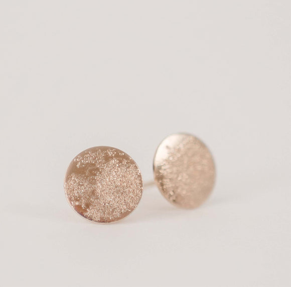 Close up photo of gold circle textured post earrings on a white table.  Handcrafted textured stardust earrings by Krista Knickerbocker Designs. 