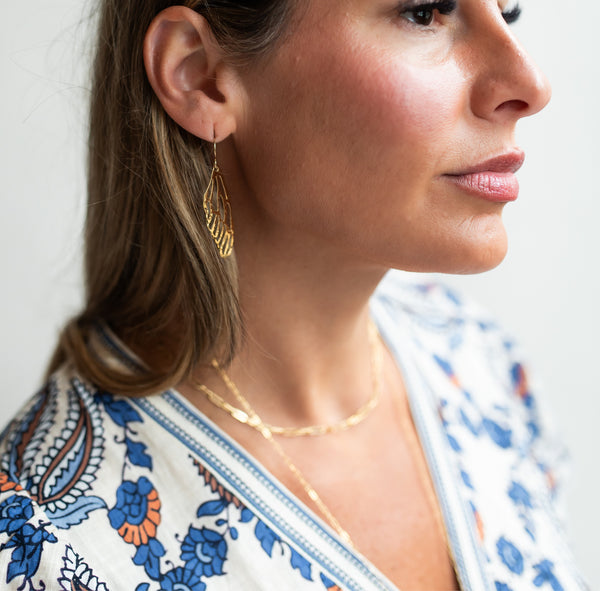 Profile of beautiful woman looking away and wearing Krista Knickerbocker Designs' gold plated dragonfly wing dangle earrings and layered everyday gold filled chains. 
