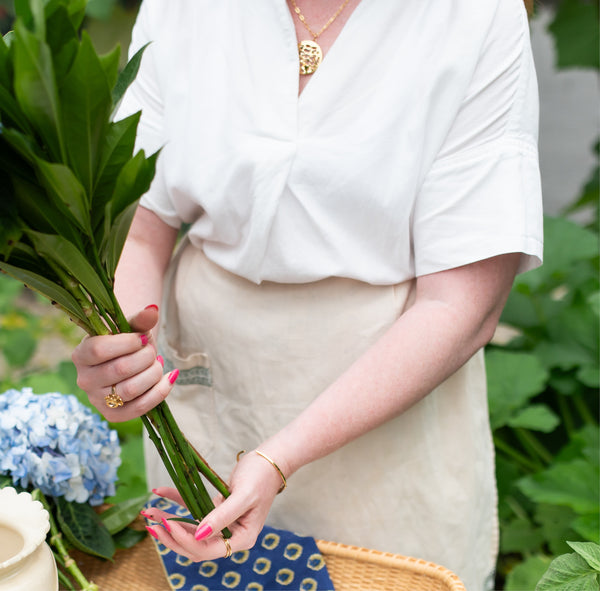 Zoom in of woman arranging flowers in a white shirt and tan apron while wearing a 14k gold vermeil cluster ring and water reflection pendant crafted by Krista Knickerbocker Designs. 