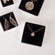 Various pieces of 14k gold vermeil handcrafted jewelry in jewelry boxes with black foam inserts, all handcrafted by Krista Knickerbocker Designs.  Pieces include dragonfly wing dangle earrings, textured circle "stardust" pendant, and layered porous water reflection necklace. 