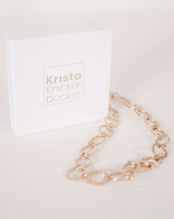 Handcrafted chunky gold chain by Krista Knickerbocker Designs on a white table in front of the gold embossed branded jewelry box with the designer's name on it. 